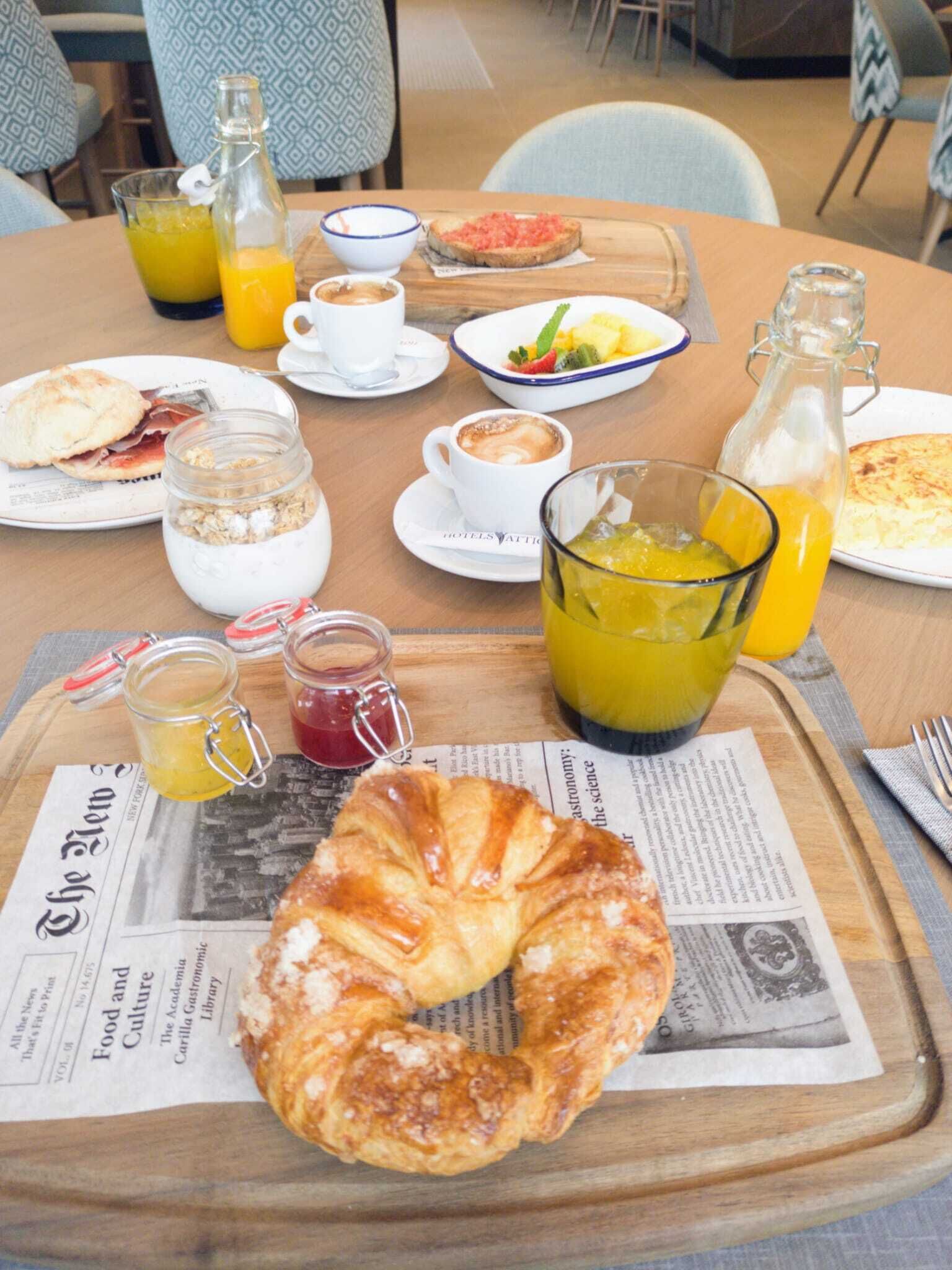 A breakfast setting with a croissant, coffee, orange juice, and various breakfast items on a table with newspapers underneath.