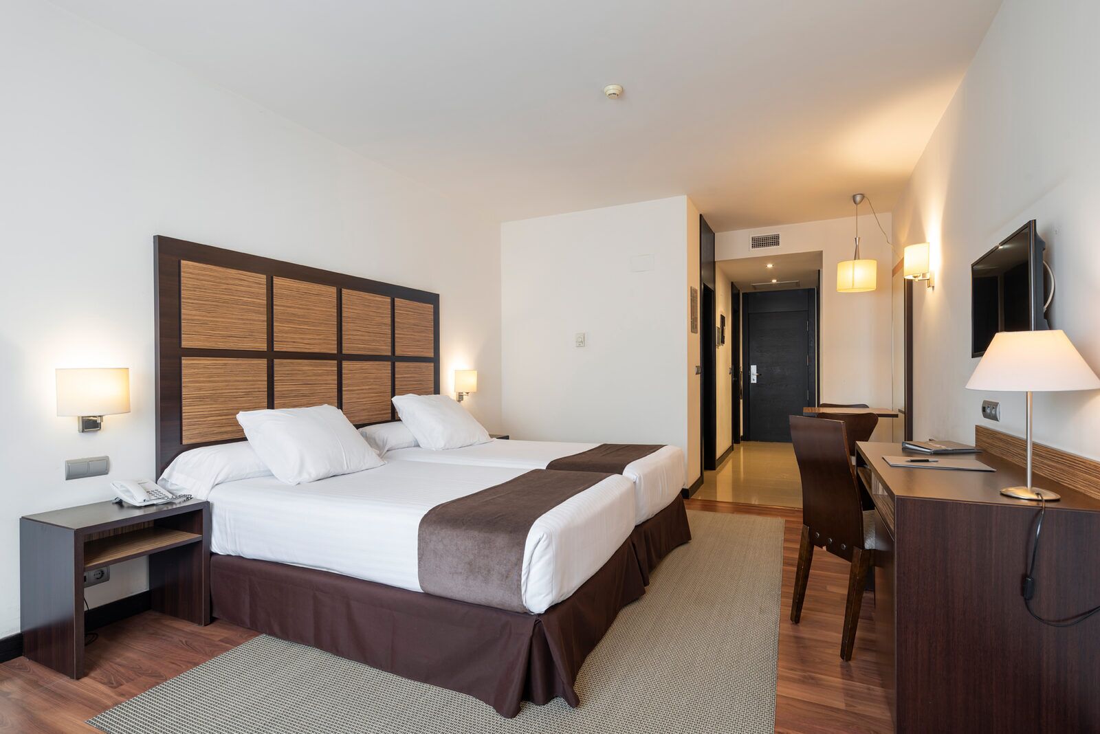 Habitación de hotel con una cama grande, mesitas de noche, escritorio, silla, televisor y lámpara.