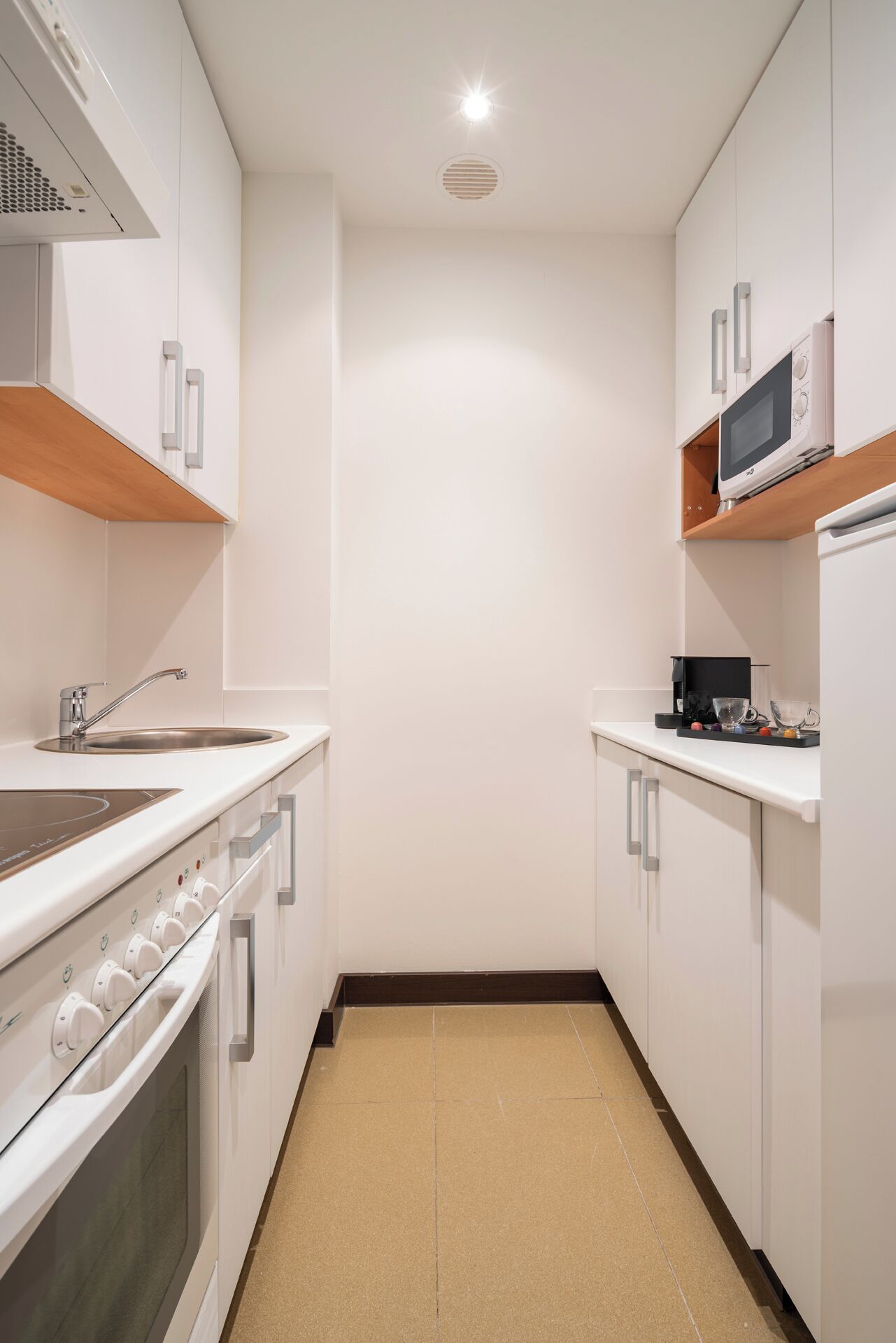 A modern kitchen with white cabinets, a stainless steel sink, a built-in oven, and a microwave on a shelf.