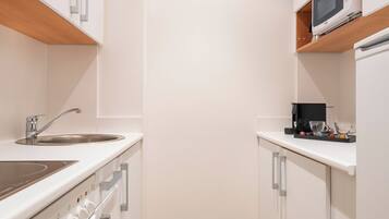A modern kitchen with white cabinets, a stainless steel sink, a built-in oven, and a microwave on a shelf.