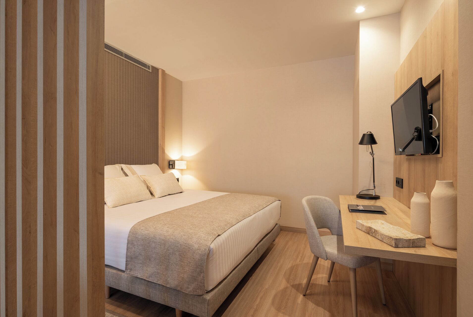Una habitación de hotel con cama, mesita de noche, lámpara, televisión y escritorio con silla.
