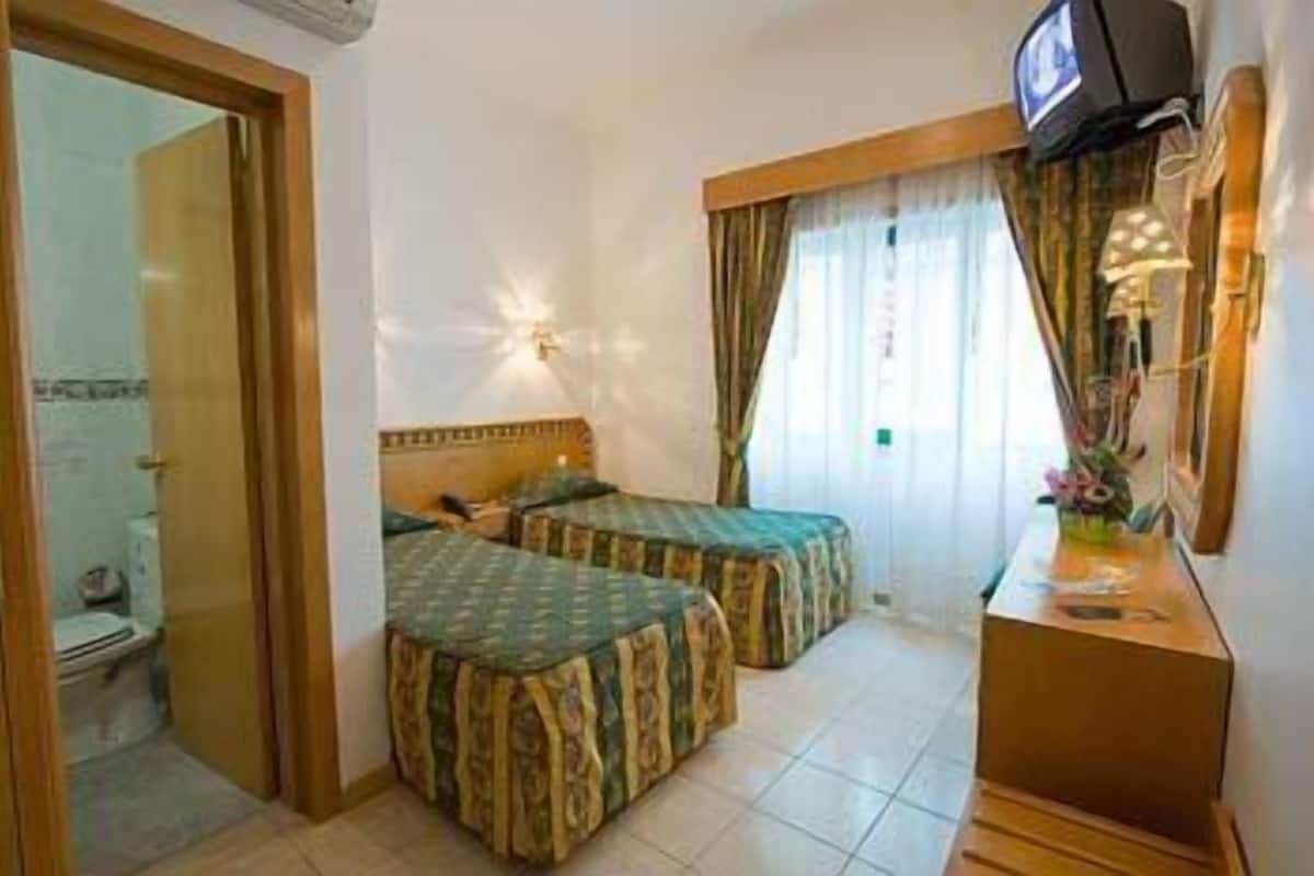 Ein Hotelzimmer mit zwei Betten, einem Fernseher und einem durch eine geöffnete Tür sichtbaren Badezimmer.