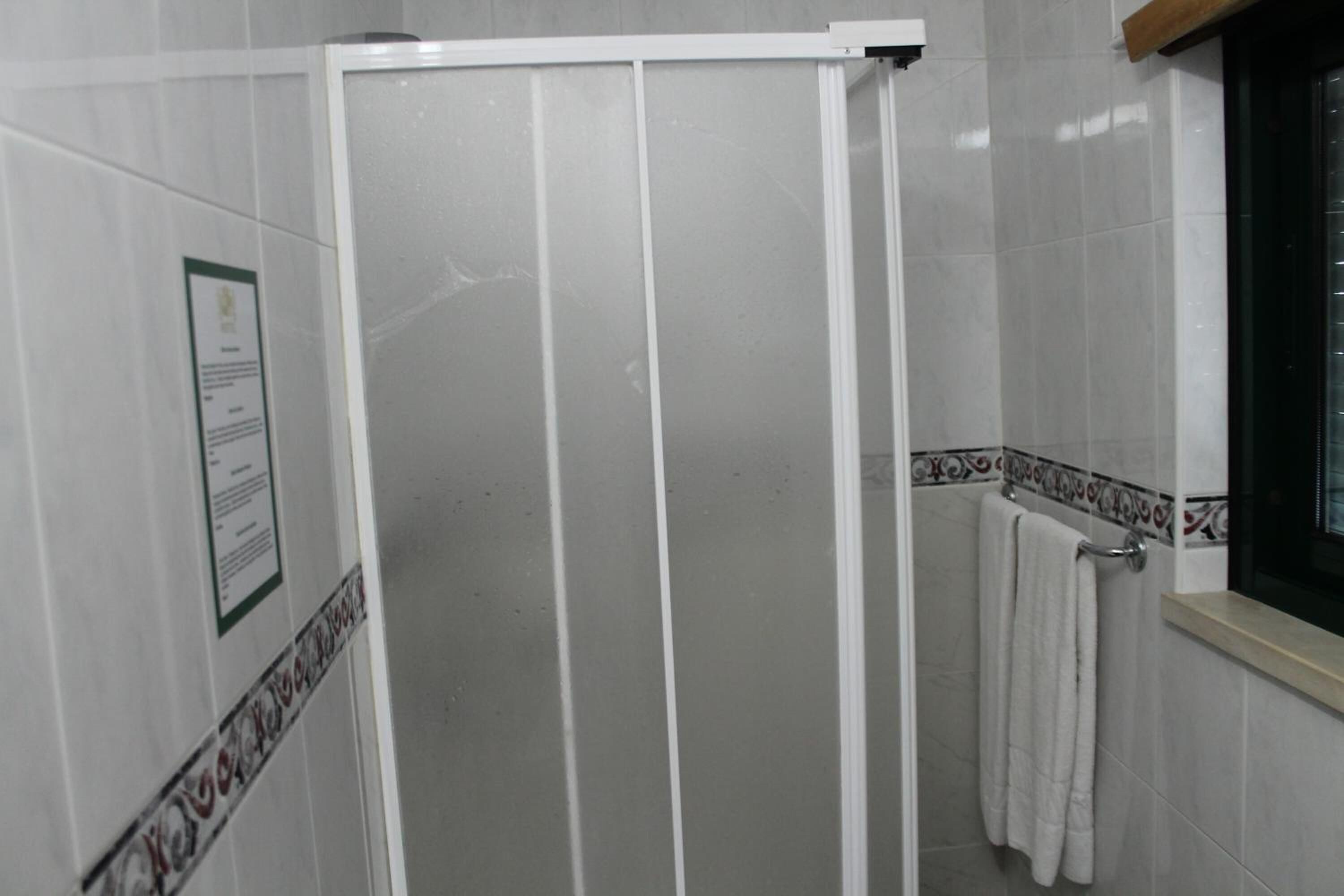 A bathroom with a white shower enclosure, a towel rack, and a window with a view.