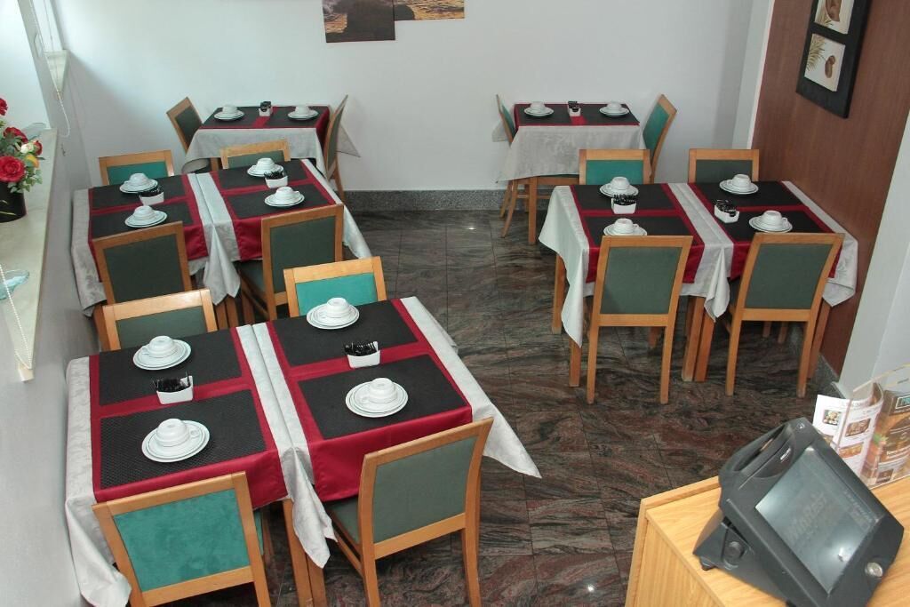 A dining area with tables set for four, each with white plates and cups, and chairs with green cushions.
