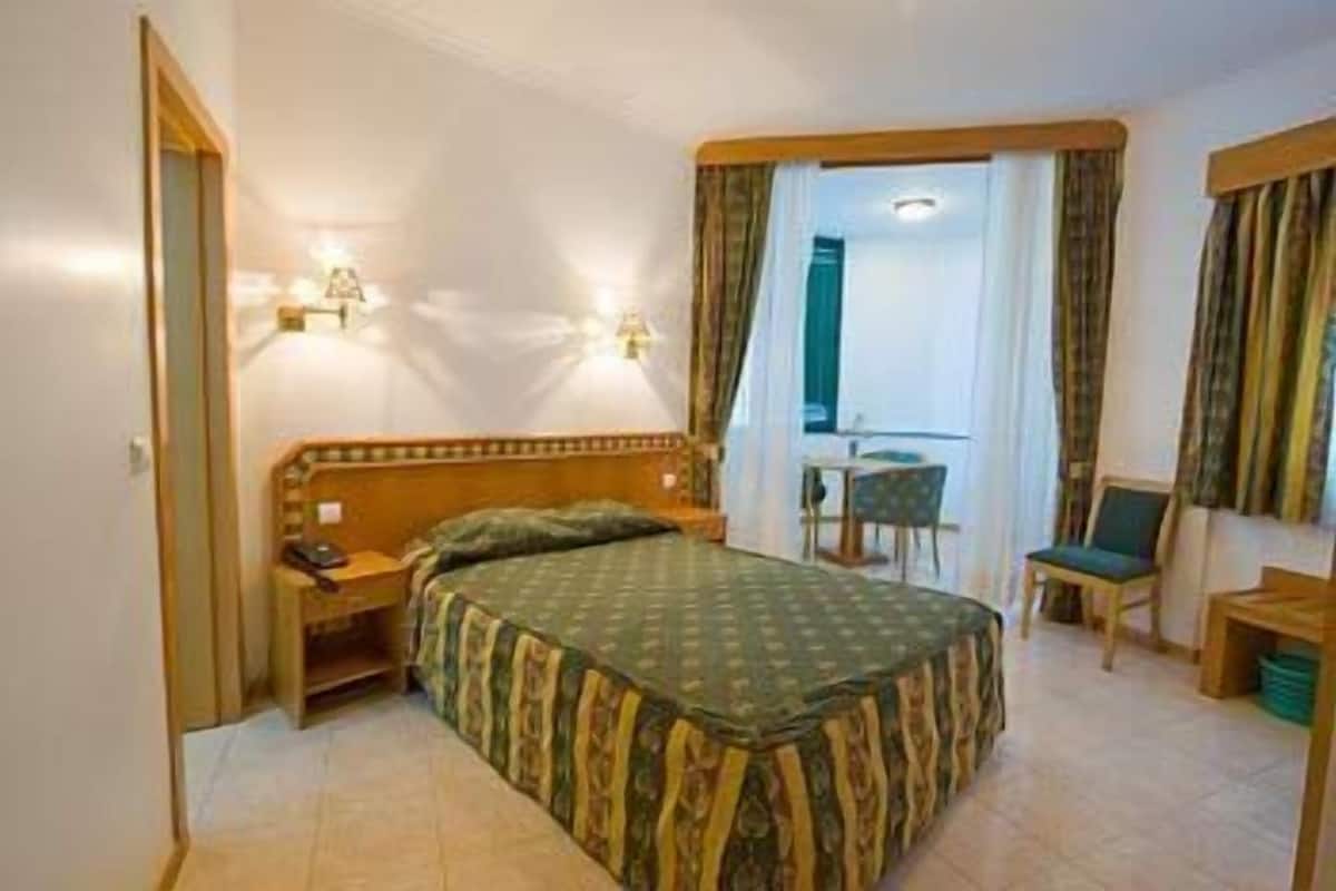 Ein Hotelzimmer mit Bett, Nachttisch, Lampe, Sessel und einem kleinen Tisch.