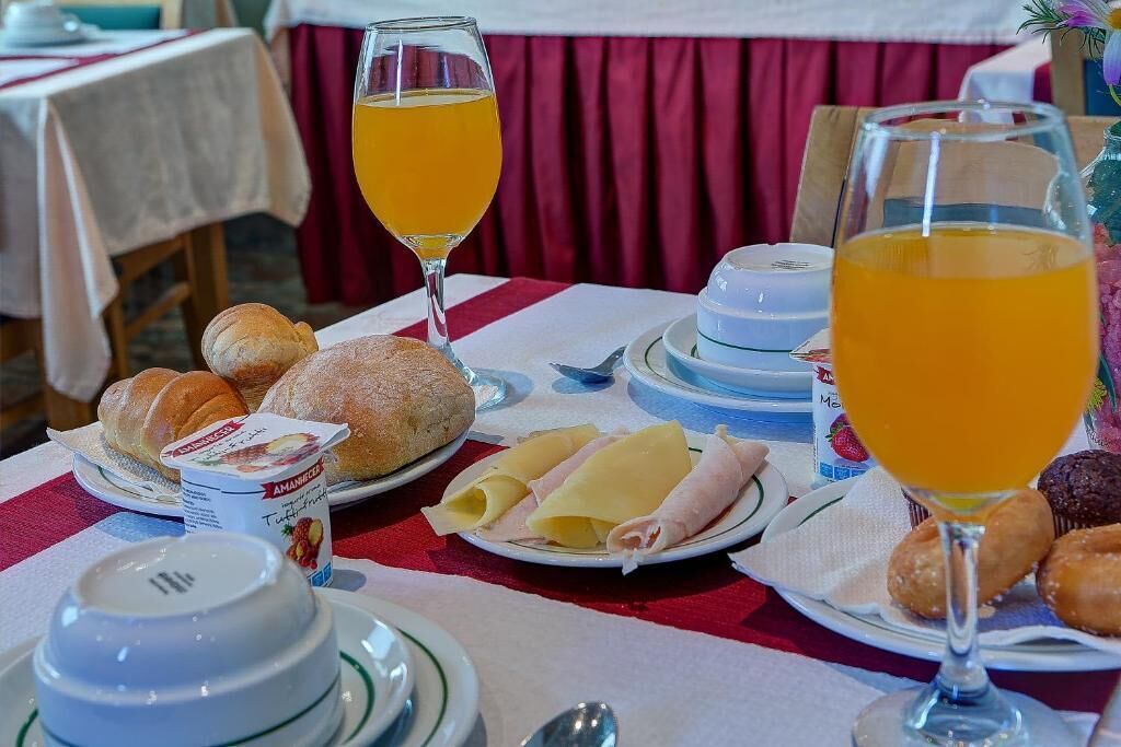 Un desayuno con cruasanes, queso, jamón y jugo de naranja sobre una mesa.
