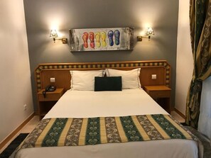 A hotel room with a large bed, two bedside tables, a wall-mounted artwork, and a curtain. - Real Caparica Hotel (Almada)