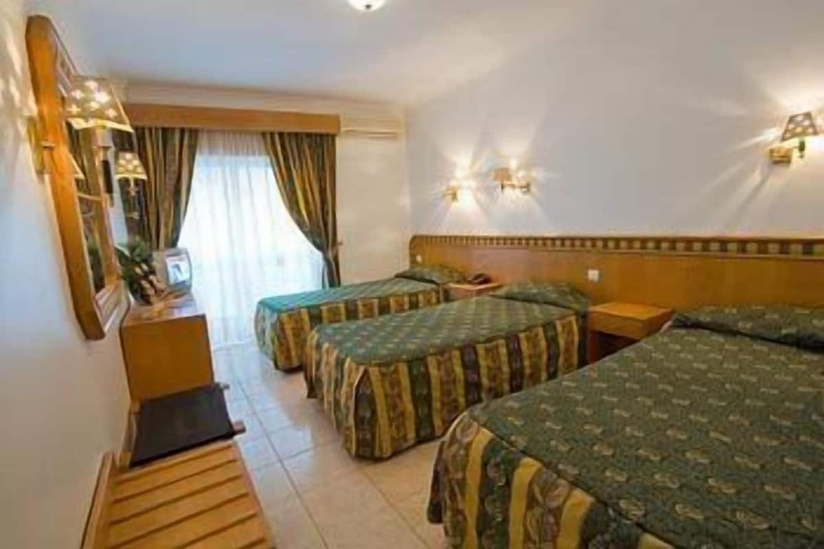 Ein Hotelzimmer mit zwei Betten, einem Schreibtisch, einem Spiegel und einem Fenster mit Vorhängen.