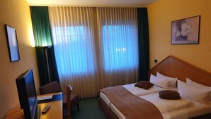 Habitació d'hotel amb llit, escriptori amb televisió, cadira i finestra amb cortines.