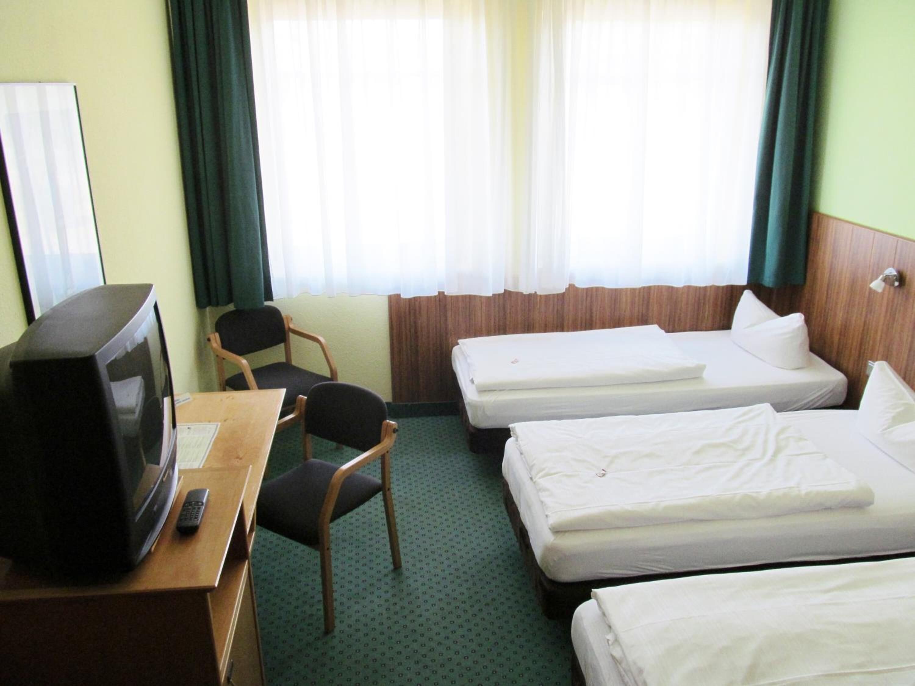A hotel room with two single beds, a desk with a television and remote control, a chair, and a window with curtains.