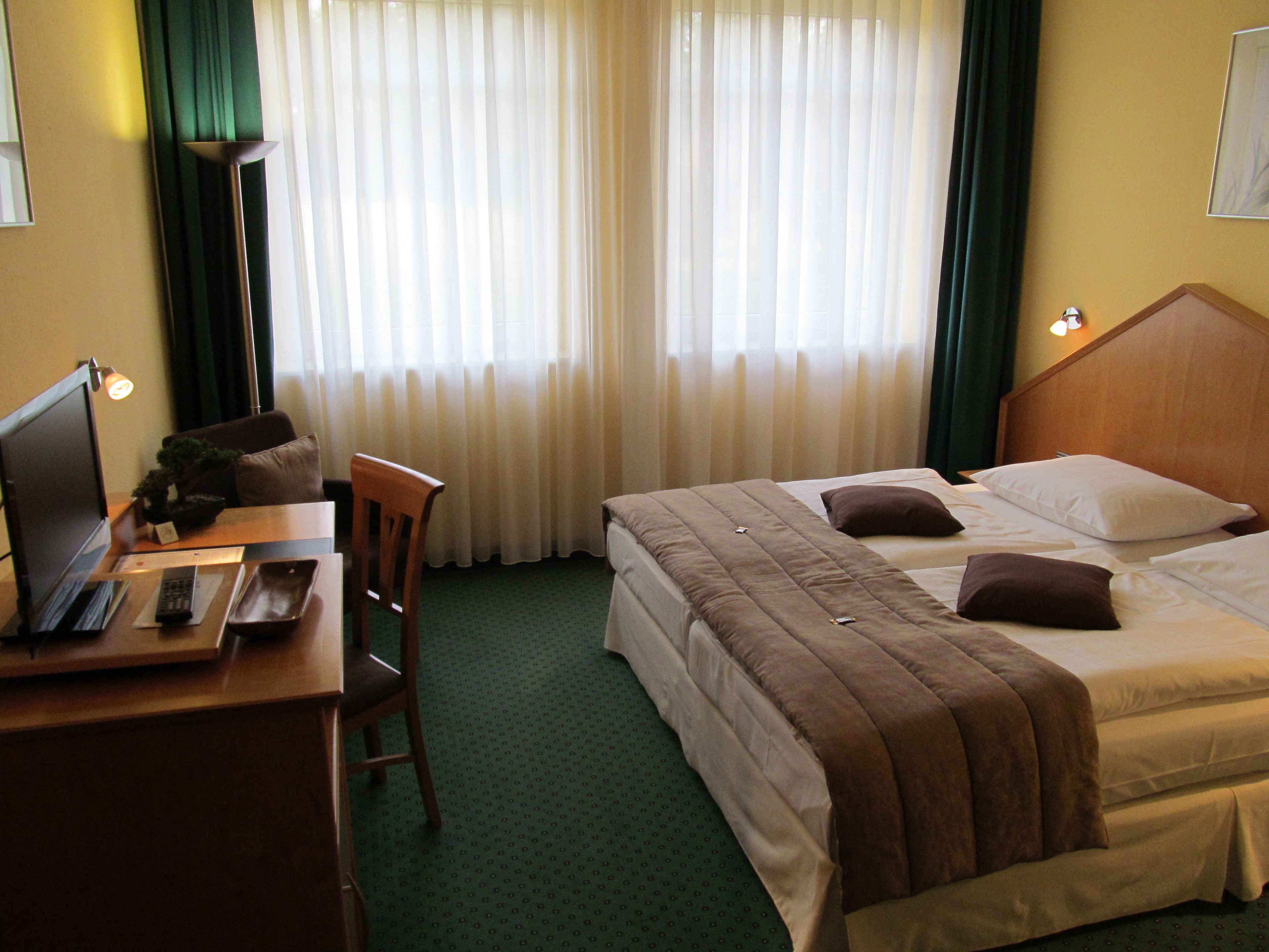 Une chambre d’hôtel avec un lit, un bureau avec un ordinateur portable, une chaise et une fenêtre avec des rideaux.