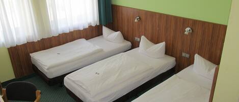 A hotel room with three single beds, a wooden headboard, a small desk with a chair, and a window with curtains.