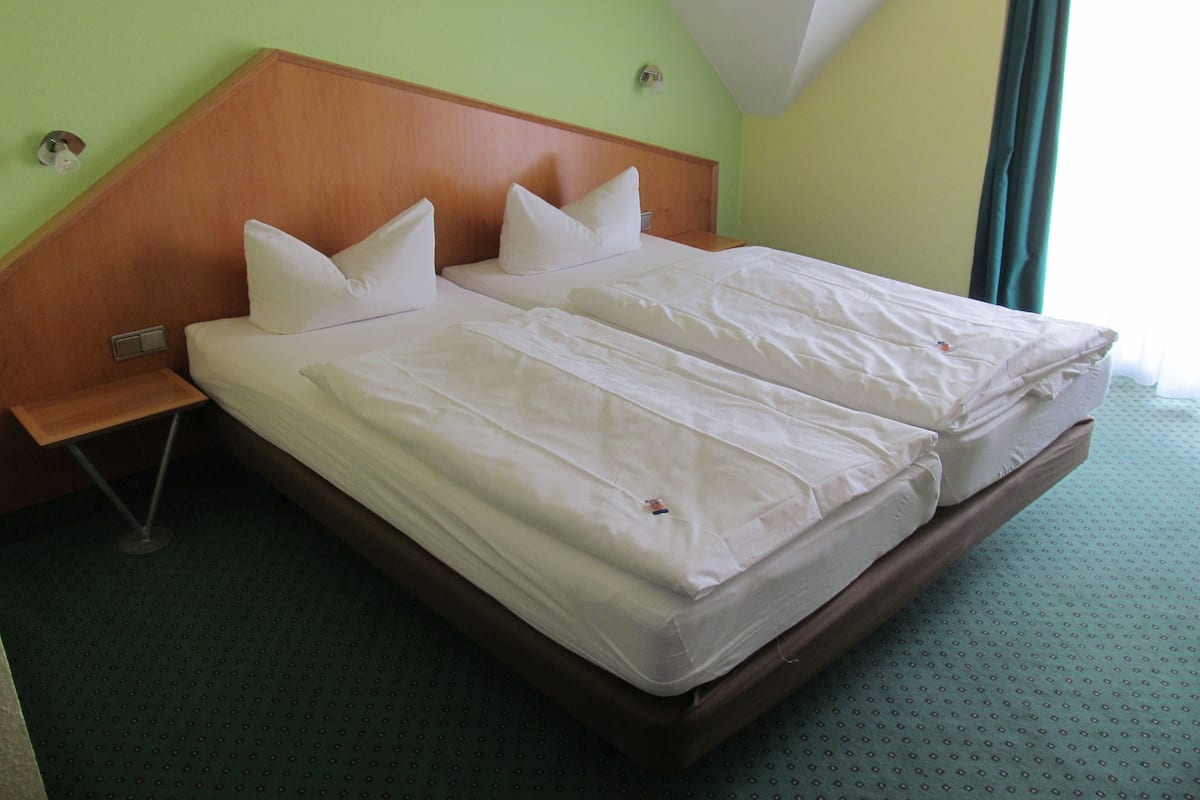 A double bed with white linens in a room with green walls and a wooden headboard.