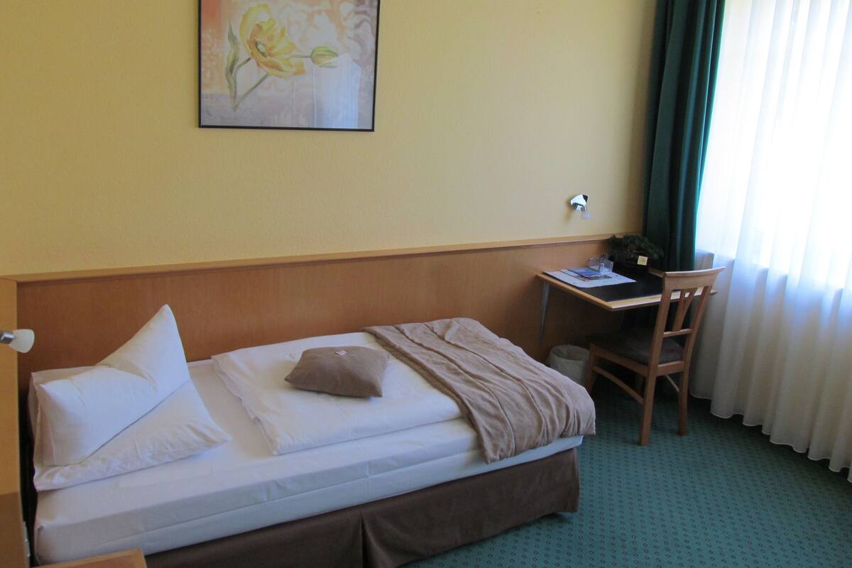 A hotel room with a bed, a desk, a chair, and a painting on the wall.