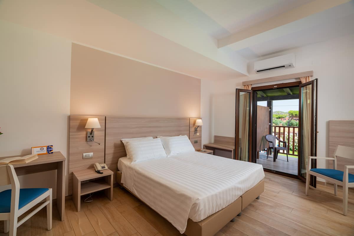 A hotel room with a bed, bedside tables, a desk, a chair, and a balcony with a view.