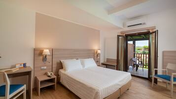 Habitación de hotel con cama, mesitas de noche, escritorio, silla y balcón con vistas.