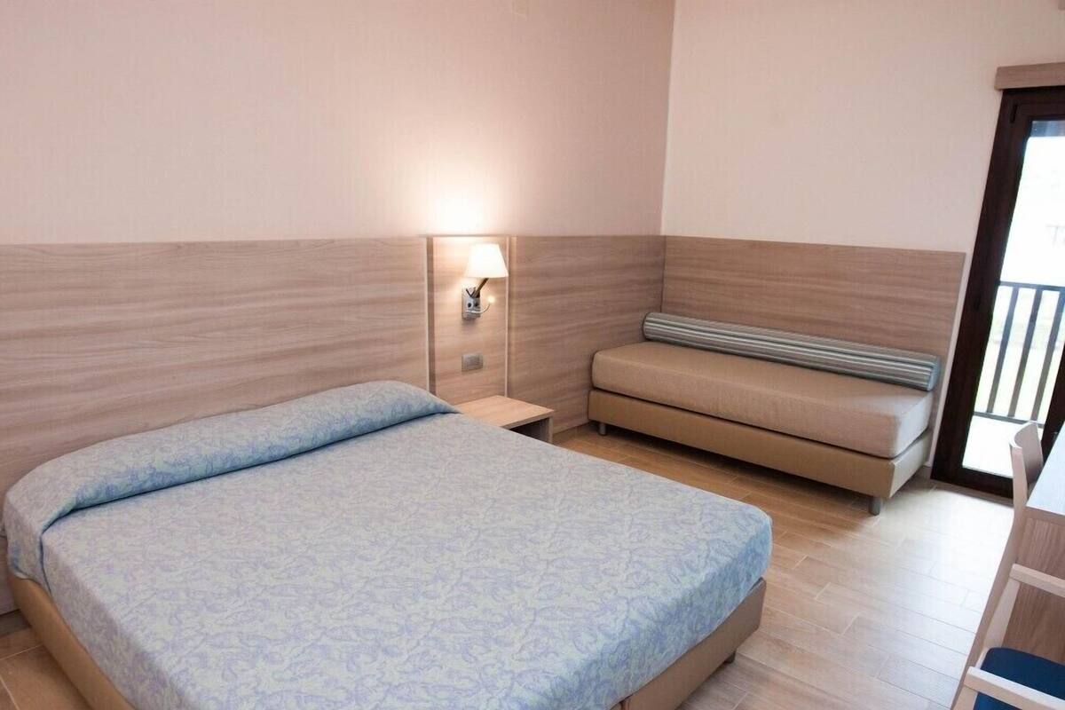 A bedroom with a bed, a nightstand, a wall-mounted lamp, and a sofa.