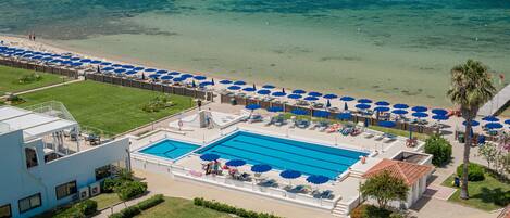 A resort with a swimming pool, beach umbrellas, and a view of the ocean.