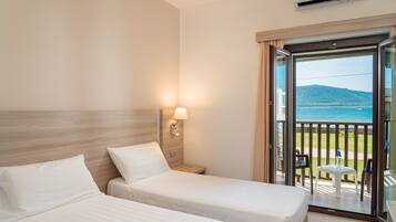 Une chambre d’hôtel avec deux lits, une table de chevet, une lampe et un balcon donnant sur la mer.