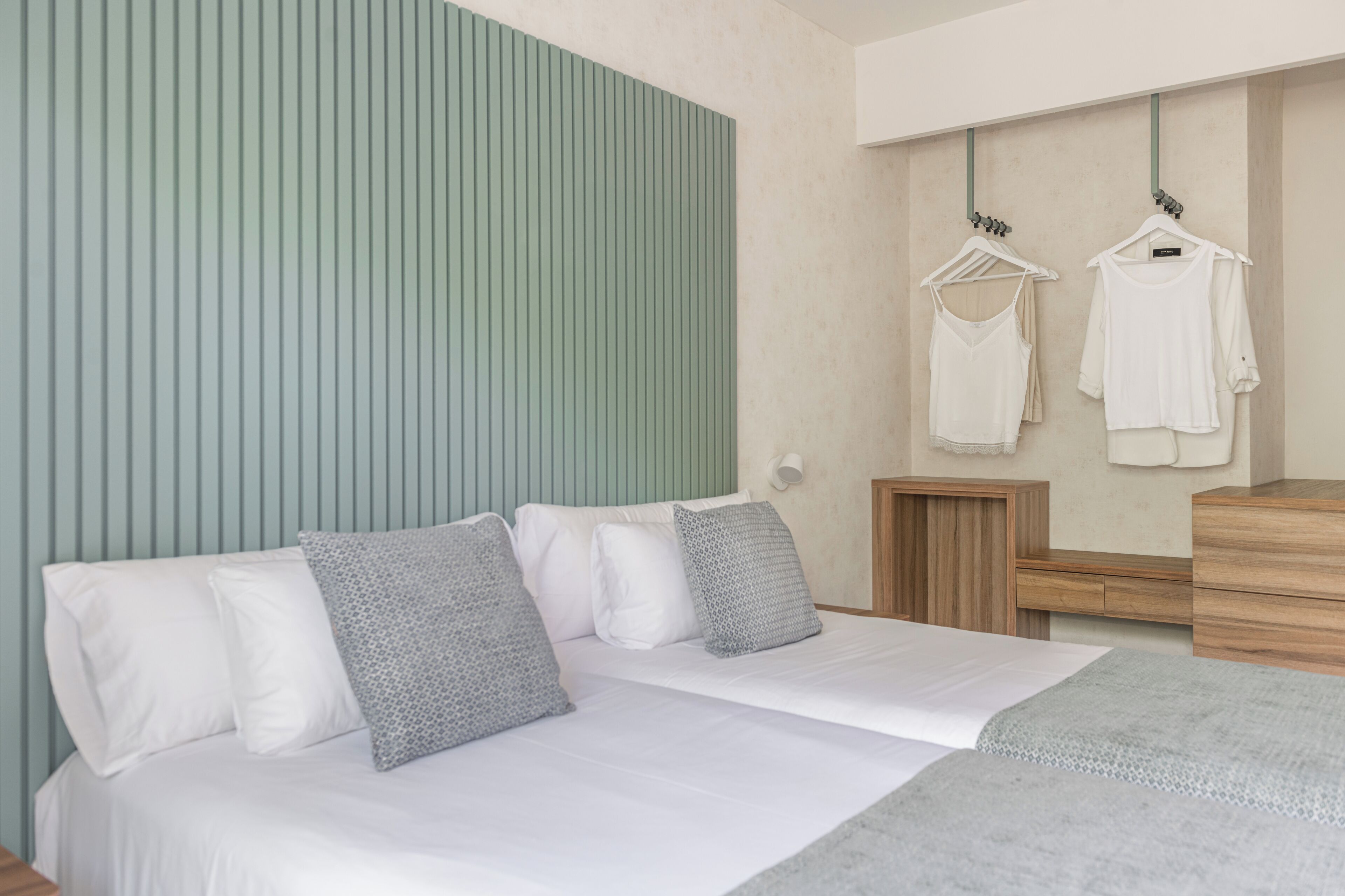 Quarto moderno com cama, almofadas, cômoda e um cabideiro fixado na parede.