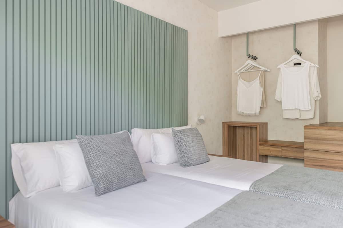 A modern bedroom with a bed, pillows, a dresser, and a wall-mounted clothing rack.