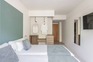 Moderni hotellihuone, jossa on suuri sänky, puinen yöpöytä, peili ja seinälle ripustettava pyyhettä kuivaava teline.