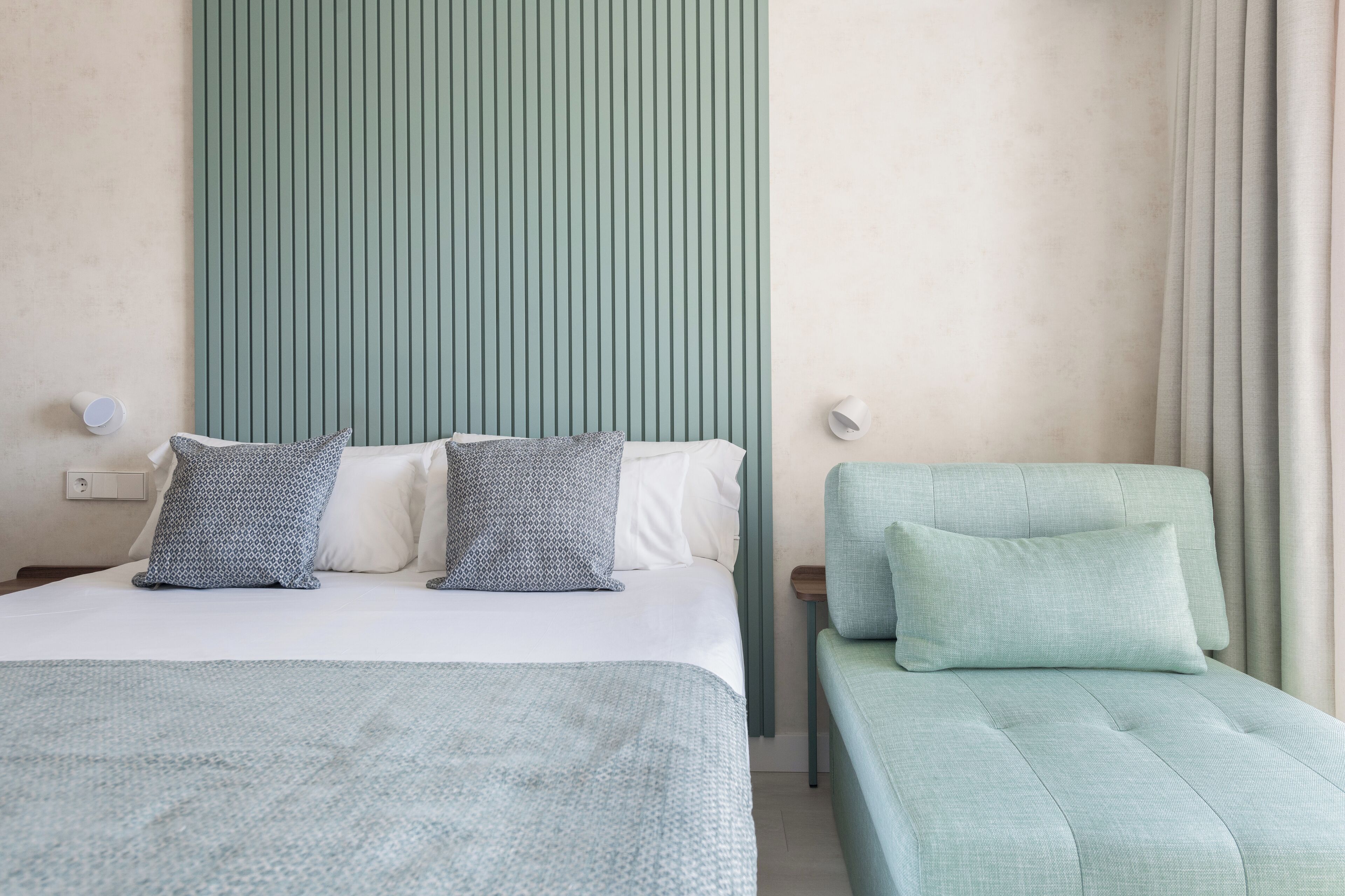 A hotel room with a bed, a nightstand, a lamp, and a window with curtains.