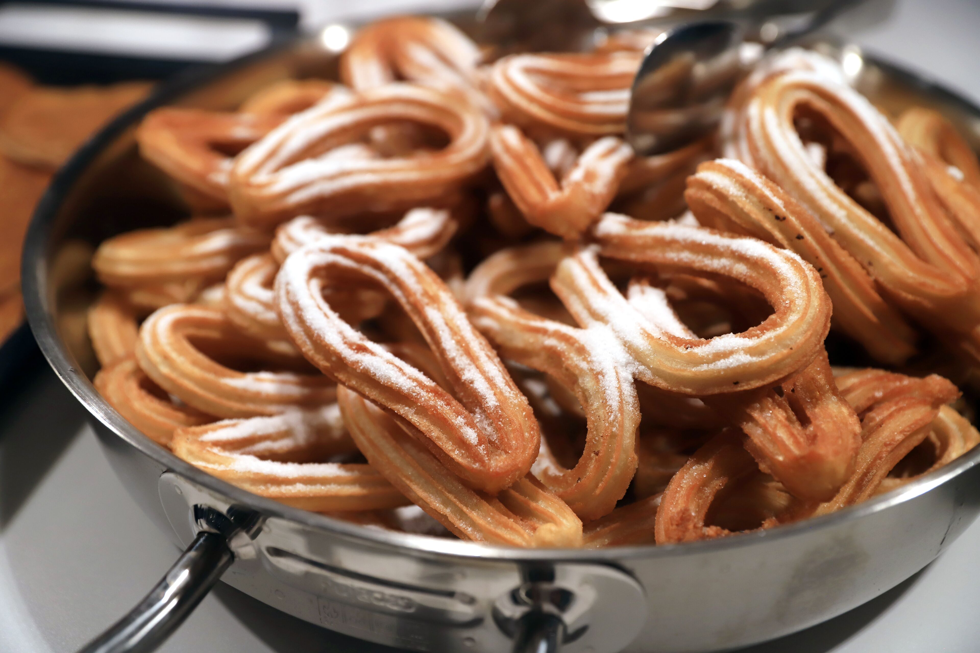 Primer plano de churros en una bandeja de metal, probablemente preparándose o sirviéndose.