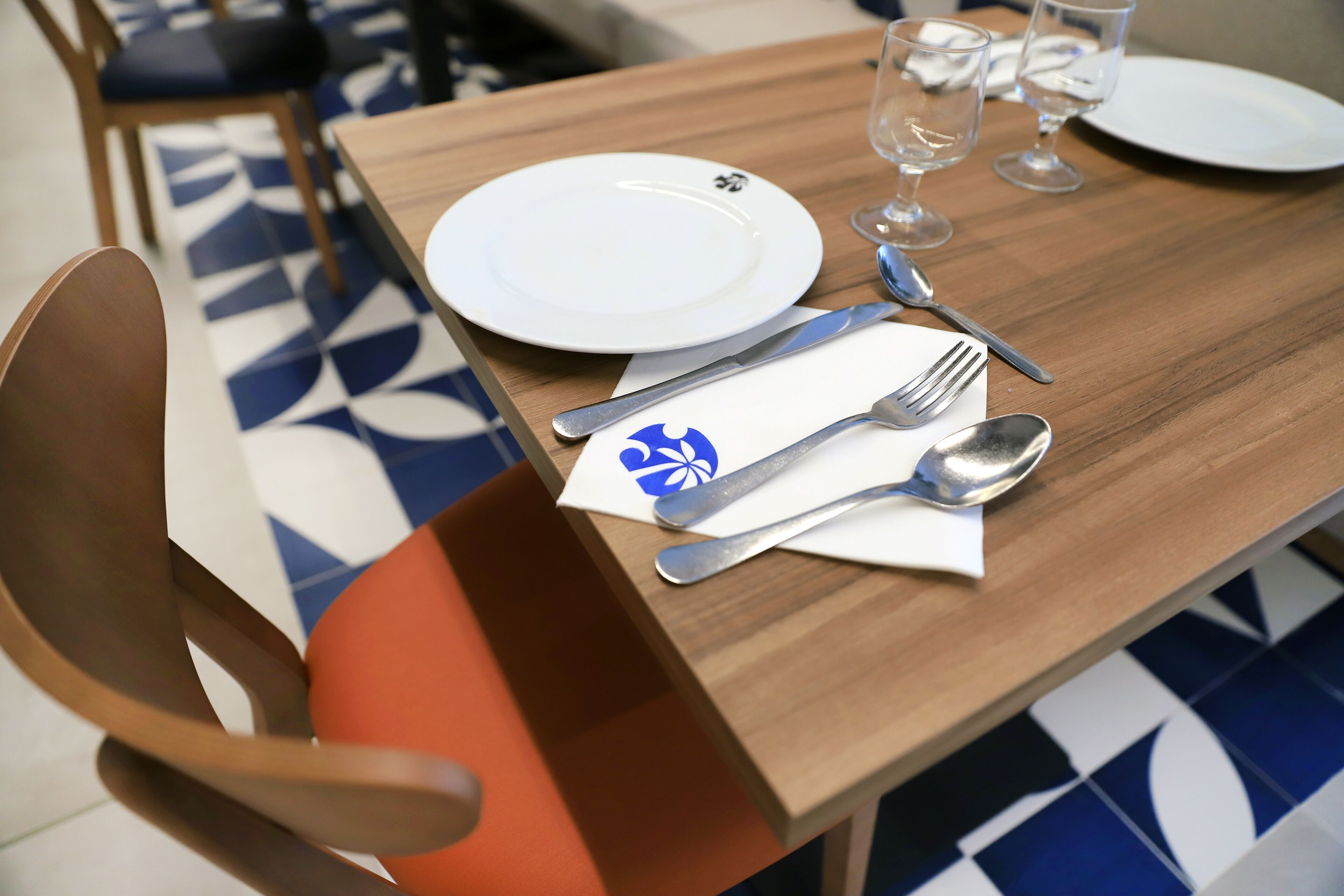 Una mesa de comedor dispuesta con platos, cubiertos y vasos, con una silla colocada junto a la mesa.