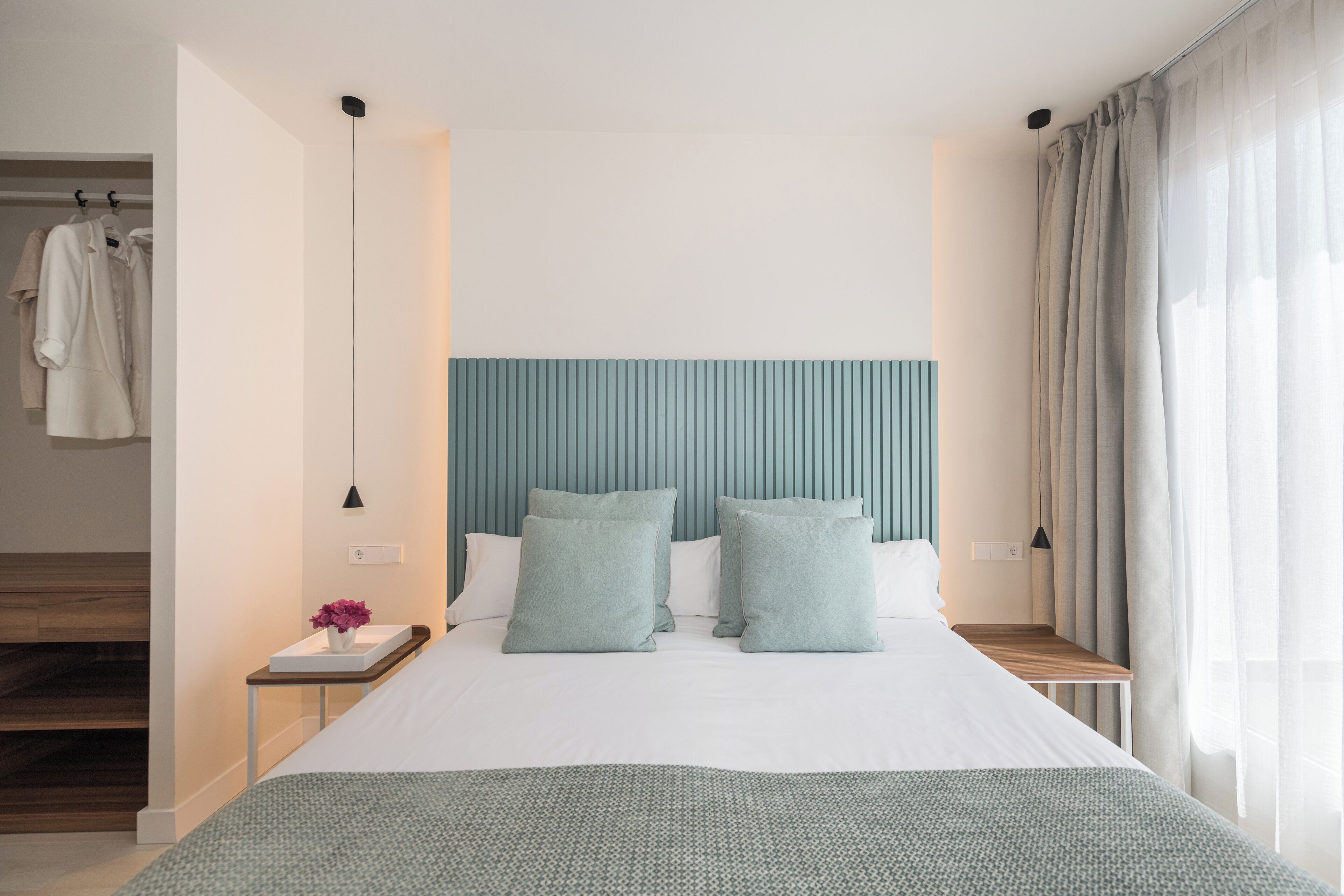 Une chambre d’hôtel moderne avec un grand lit, une tête de lit, une table de chevet, une commode et une fenêtre avec des rideaux.