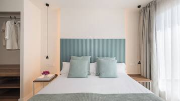 Une chambre d’hôtel moderne avec un grand lit, une tête de lit, une table de chevet, une commode et une fenêtre avec des rideaux.