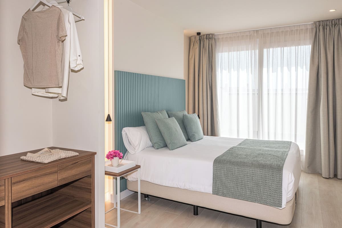 Ein modernes Hotelzimmer mit einem Bett, einem Holzschrank und einem Nachttisch mit einer Lampe.
