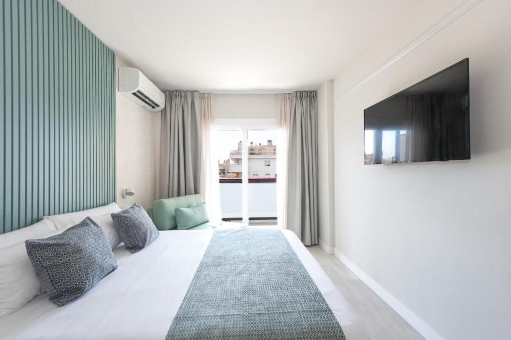 Quarto de hotel com cama, televisão, janela e vista para edifícios.