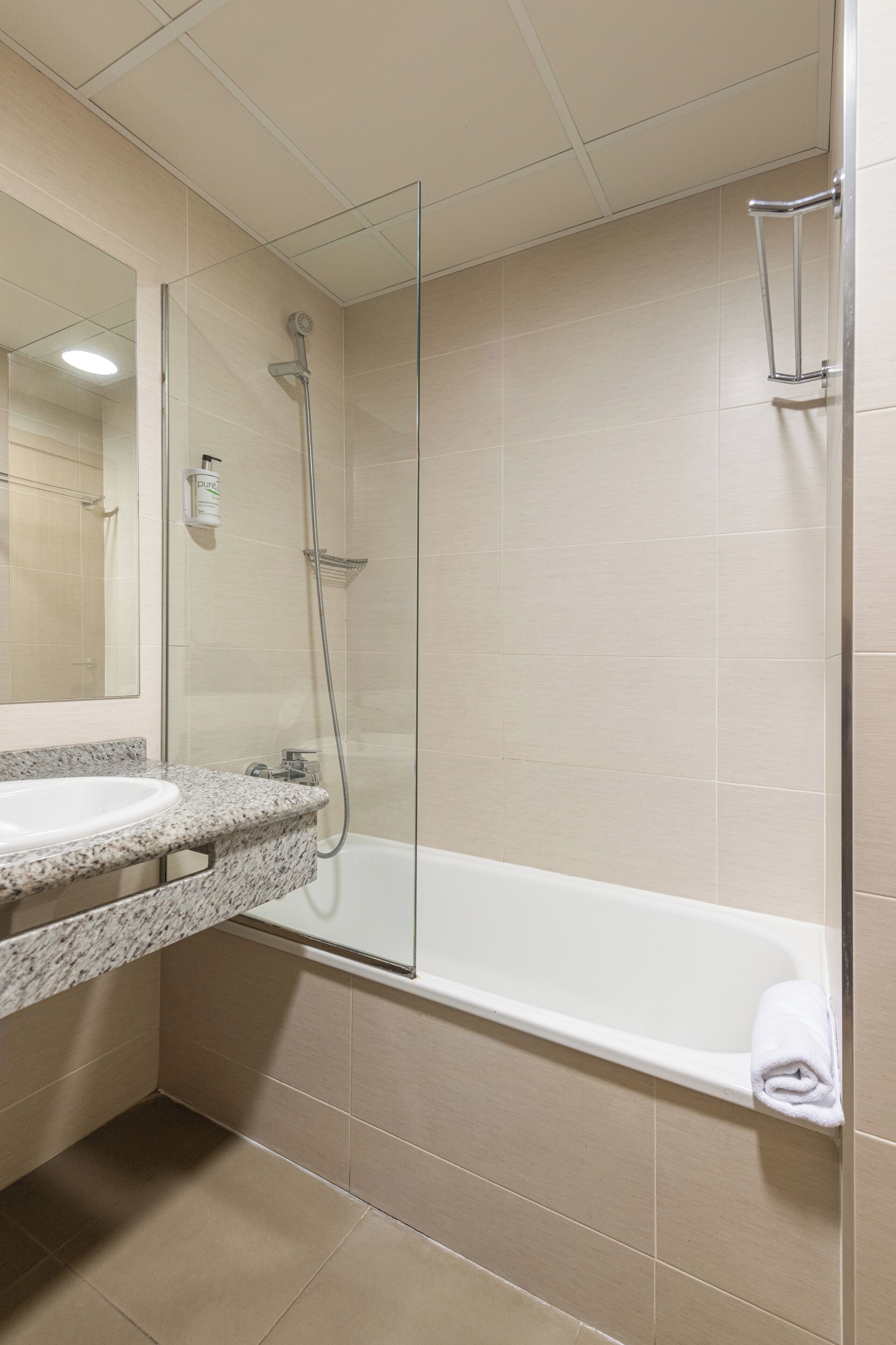 A bathroom with a glass-enclosed shower, a white bathtub, and a granite countertop sink.