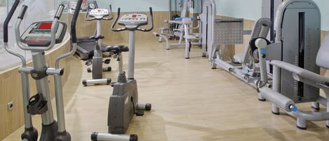 A gym with various exercise machines, a television screen, and a wooden floor.