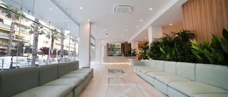 A modern lobby with a long seating area, a reception desk, and large windows overlooking a busy street.