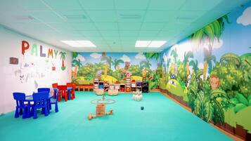 Une salle de classe ornée d’une fresque murale, avec des chaises bleues et rouges, et du matériel pédagogique.