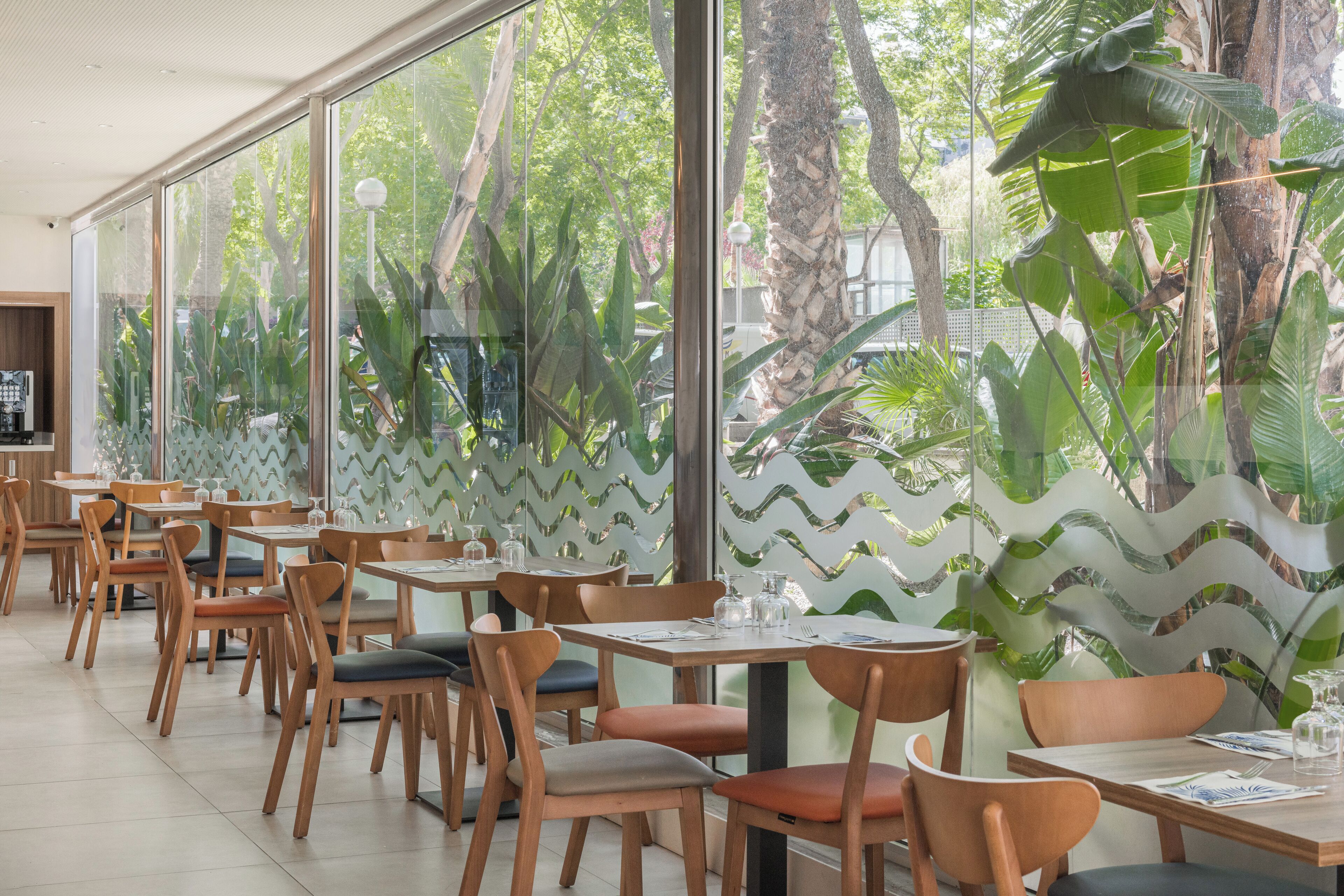 Un restaurant amb taules i caires de fusta, grans finestres i vista a zones verds a l'exterior.