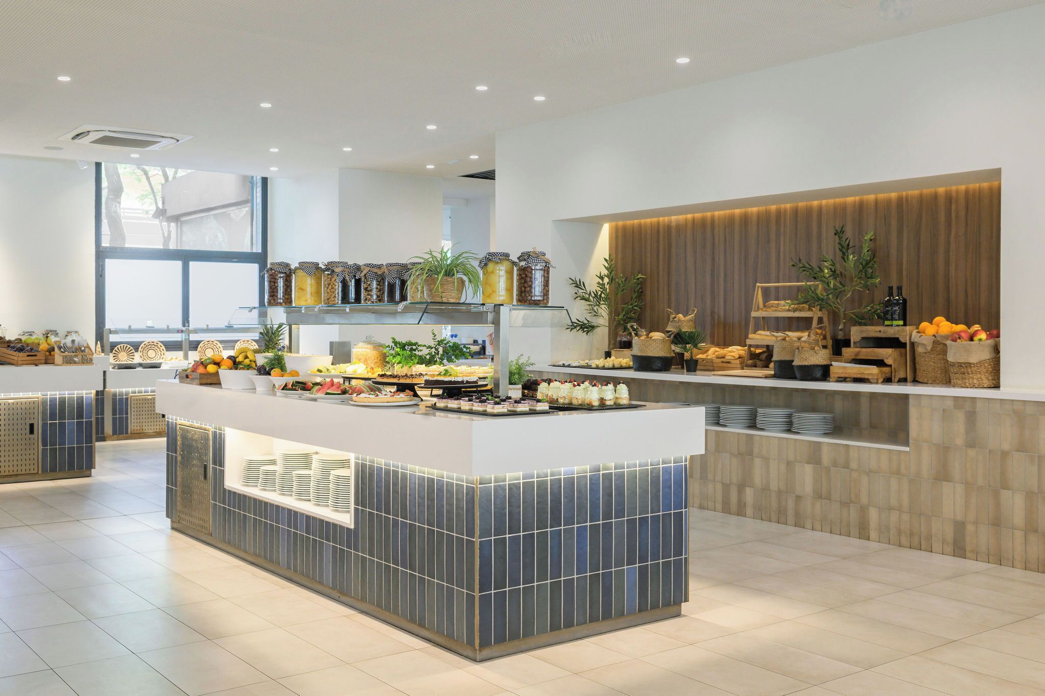 A modern reception area with a central counter displaying food items, a wooden accent wall, and a large window providing natural light.