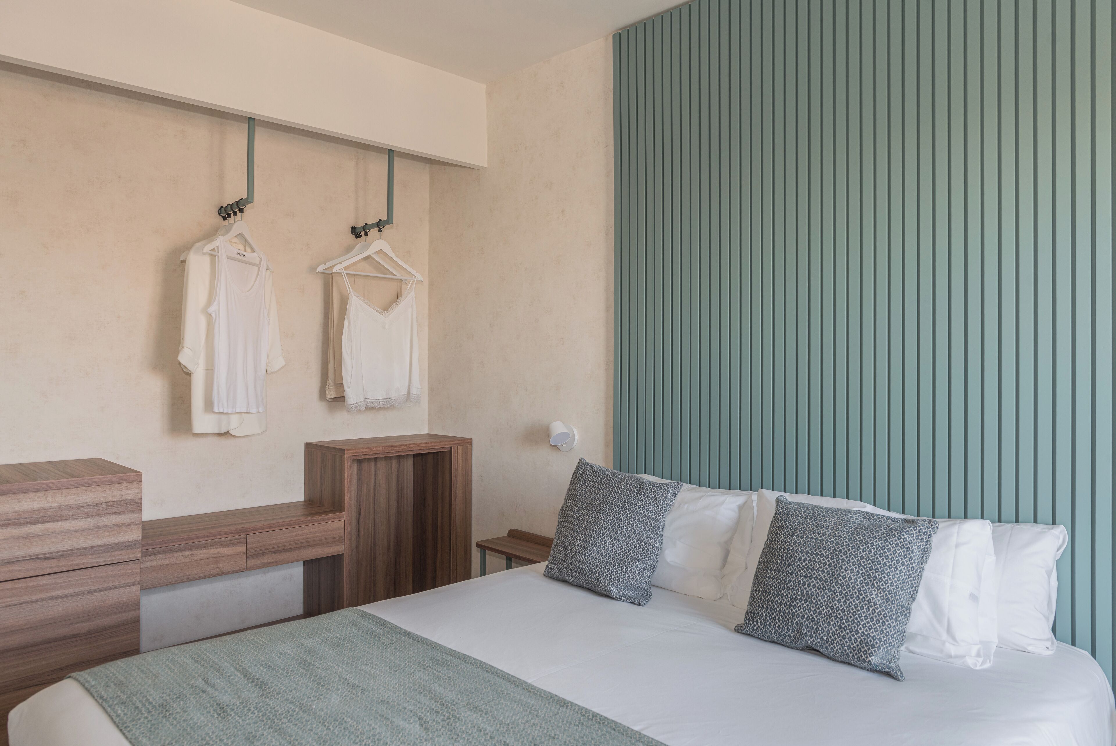 A bedroom with a bed, a wooden dresser, a bench, and a wall-mounted towel rack with two white towels.