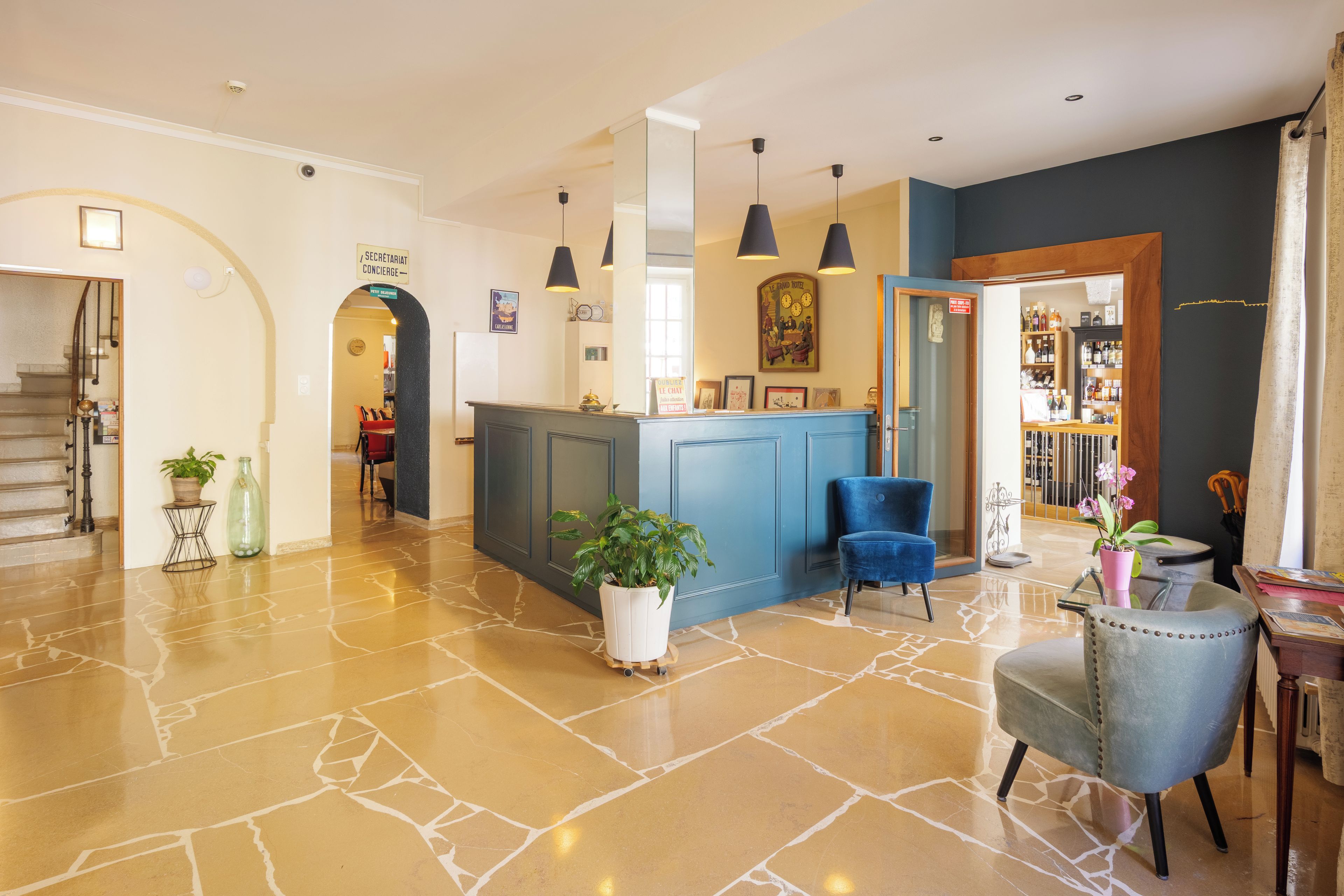 Un vestíbulo de hotel con una mesa de recepción, una escalera y un área de descanso con una silla azul.