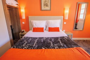 Habitación de hotel con cama, dos almohadas, mesita de noche, lámpara, espejo y ventana con cortinas.