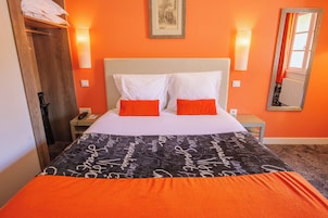 Habitación de hotel con cama, dos almohadas, mesita de noche, lámpara, espejo y ventana con cortinas.