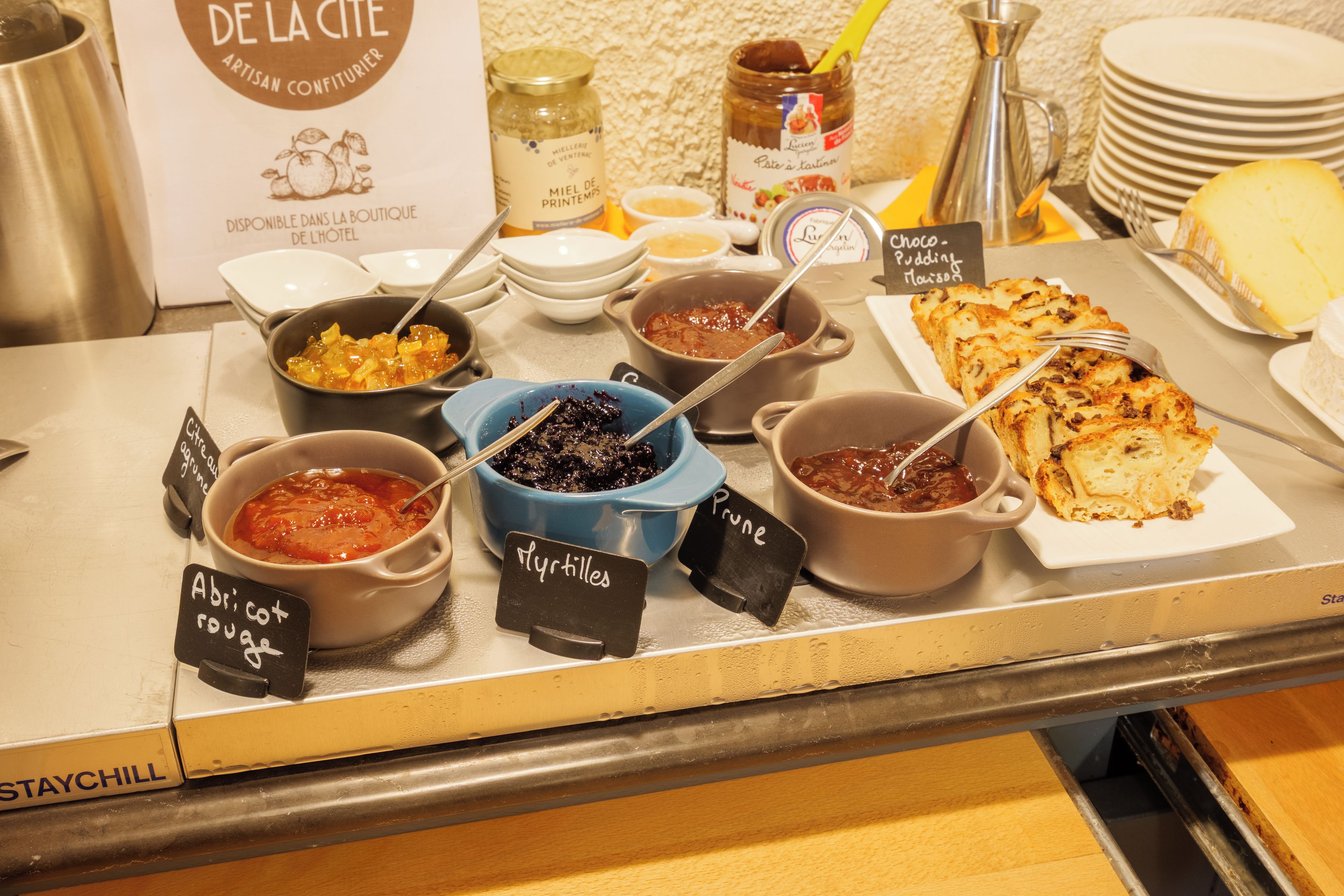 Un buffet proposant une variété de plats et d’accompagnements, notamment des pots de confitures et un panneau indiquant « pruneaux ».