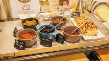 Ein Buffet mit verschiedenen Speisen und Beilagen, darunter Gläser mit Marmelade und ein Schild mit der Aufschrift 'Pflaume'.