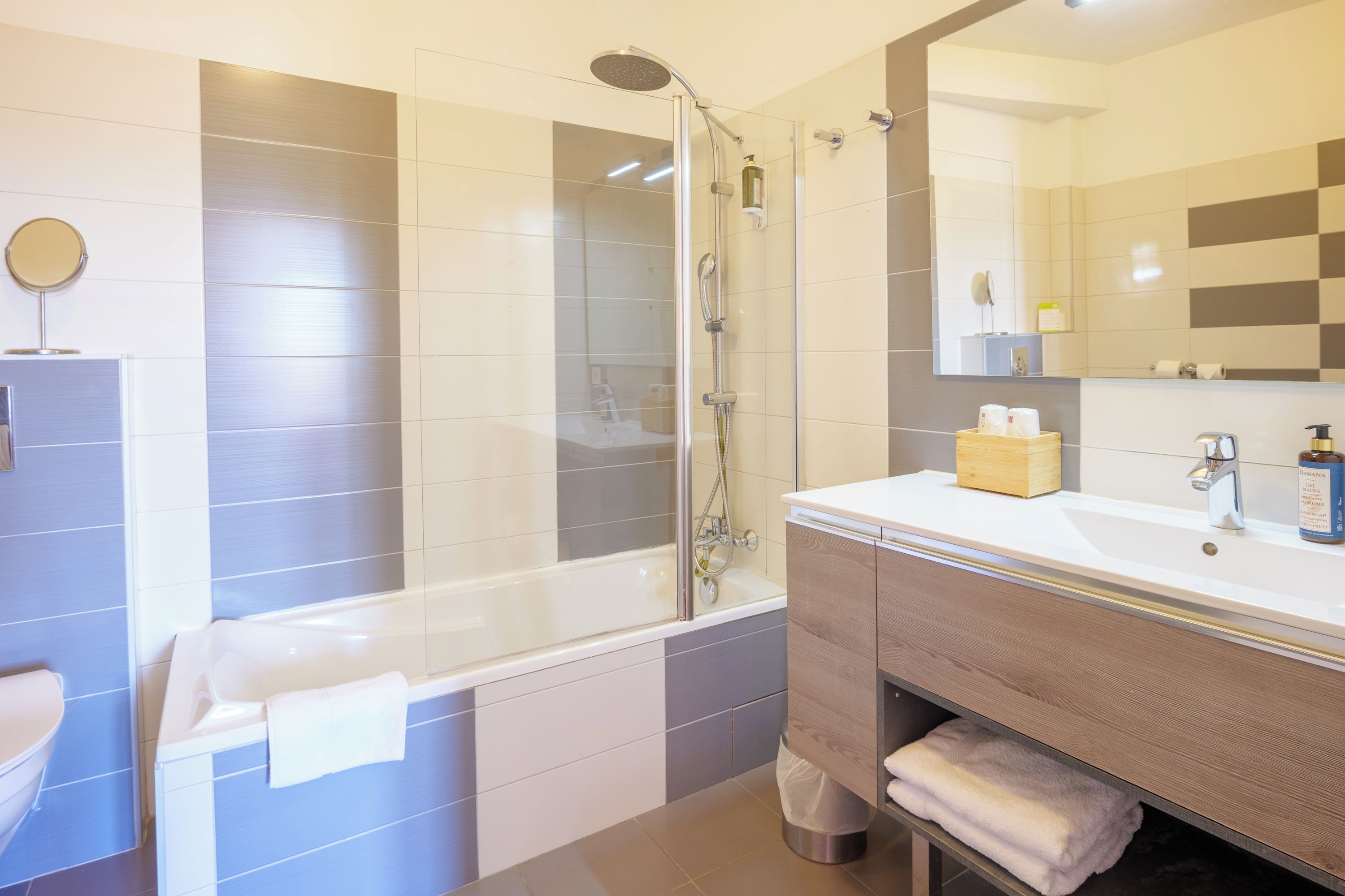 A modern bathroom with a glass-enclosed shower, a white sink with a wooden vanity, and a large mirror.