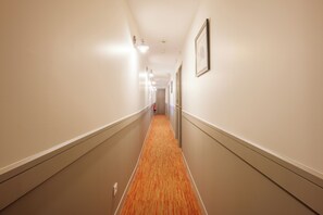 Un pasillo de hotel con pisos alfombrados, luminarias y cuadros en las paredes.