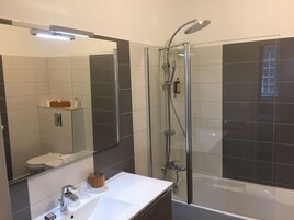 Un baño moderno con cabina de ducha de vidrio, un espejo grande y un lavabo blanco.