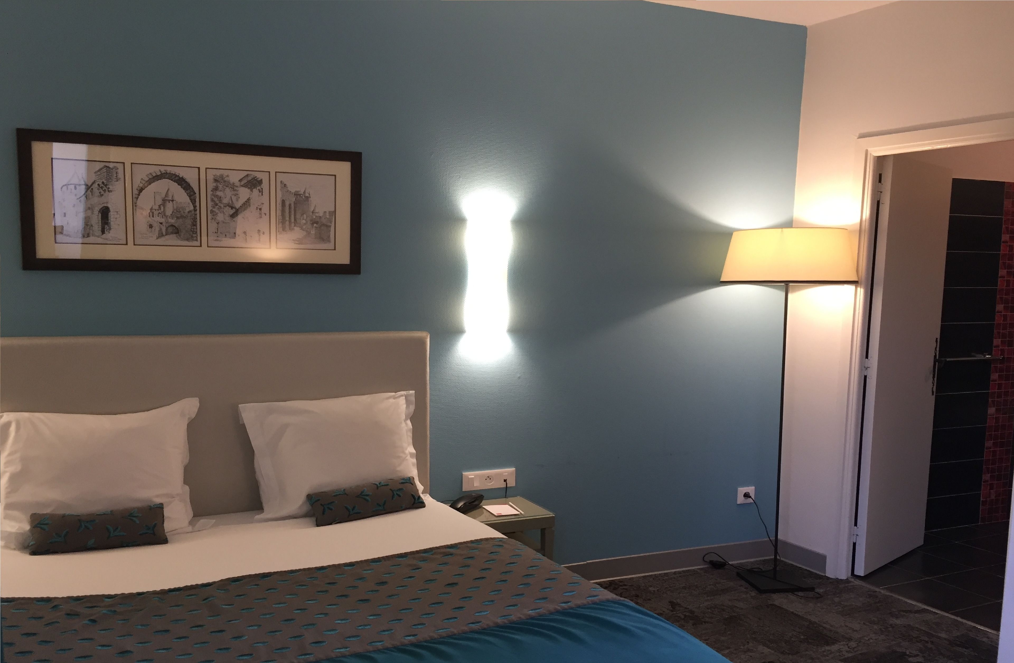 Habitación de hotel con cama, mesita de noche, lámpara y un cuadro en la pared.