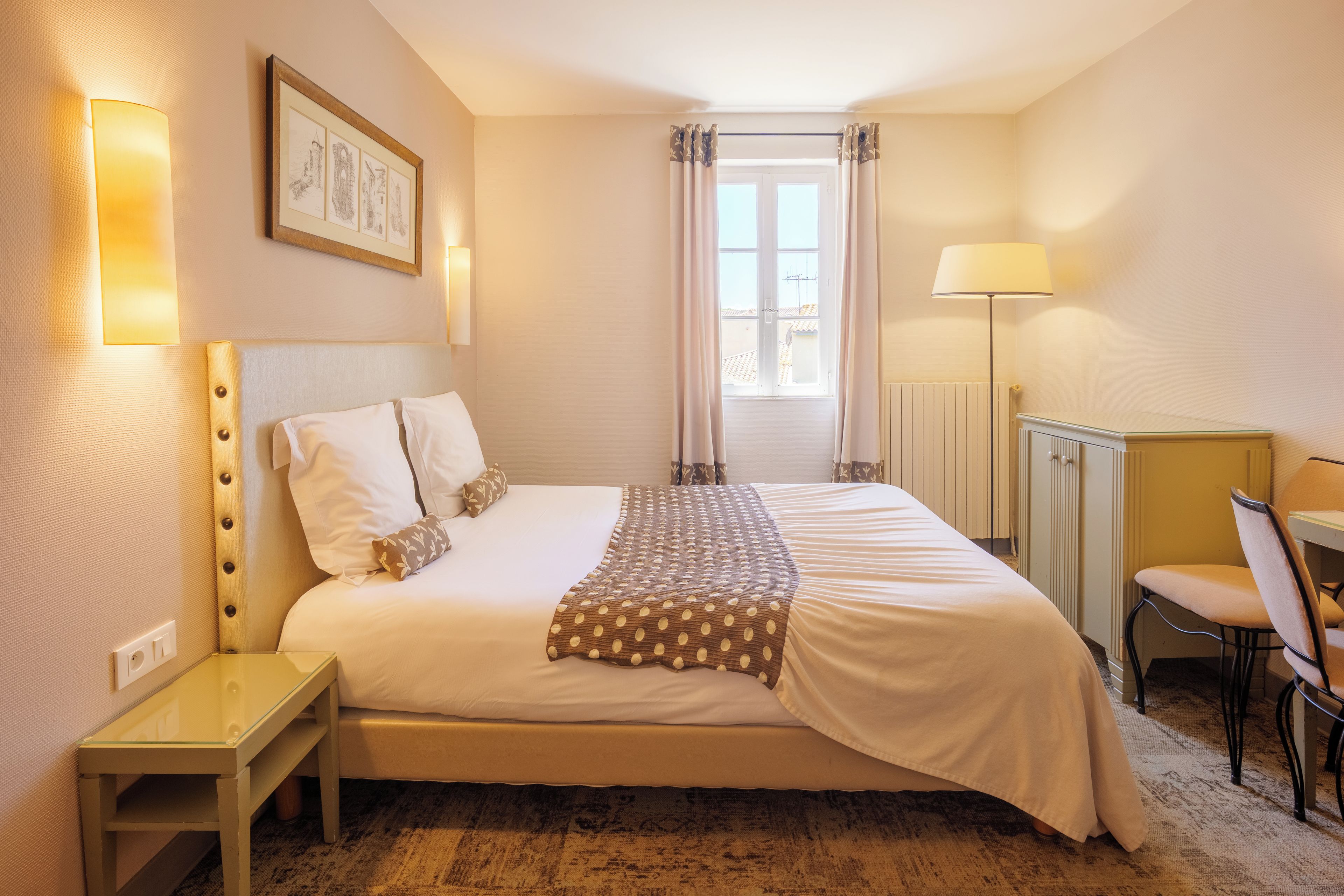 A hotel room with a bed, bedside table, lamp, chair, and a window with curtains.